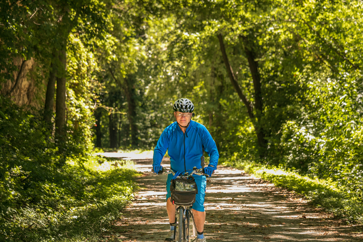 Senior man bicyclist in blue jersey riding on Midwestern trail in summer