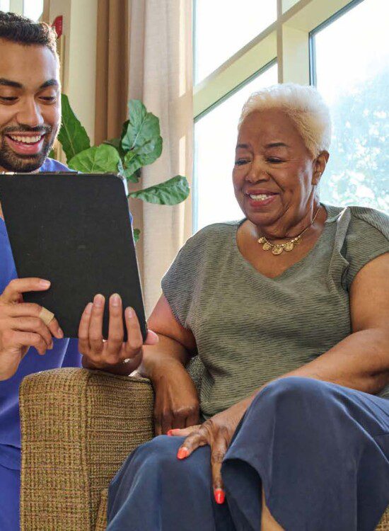 senior woman smiles while sitting in a chair discussing her health plan with a care worker