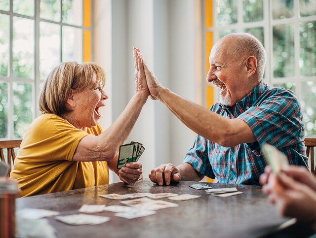 Senior man and senior woman playing cards and high-fiving each other