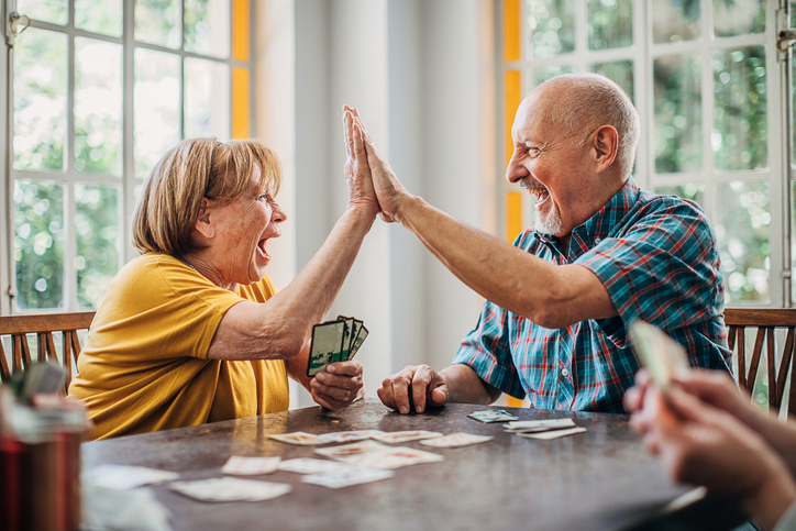 Senior man and senior woman playing cards and high-fiving each other